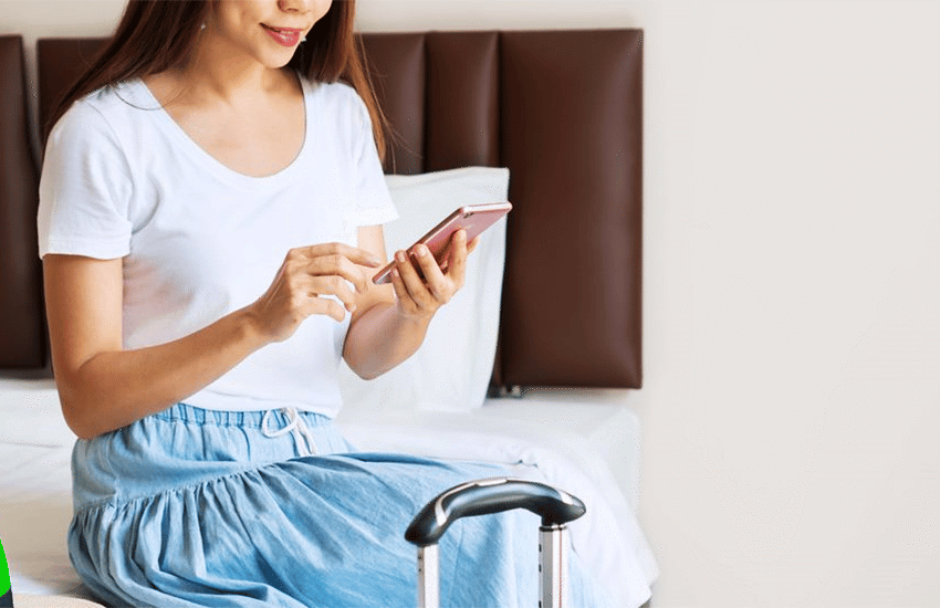 A woman using her smartphone in a hotel room, illustrating remote identity verification and document signing while travelling